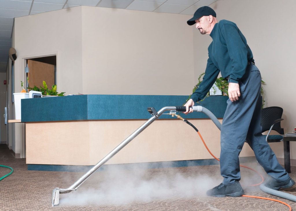 Professional carpet cleaner using steam cleaning equipment in a commercial space, demonstrating advanced cleaning techniques.